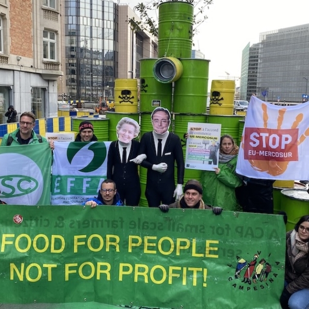 A groups of people holding protest banners standing in front of a stack of oil barrels