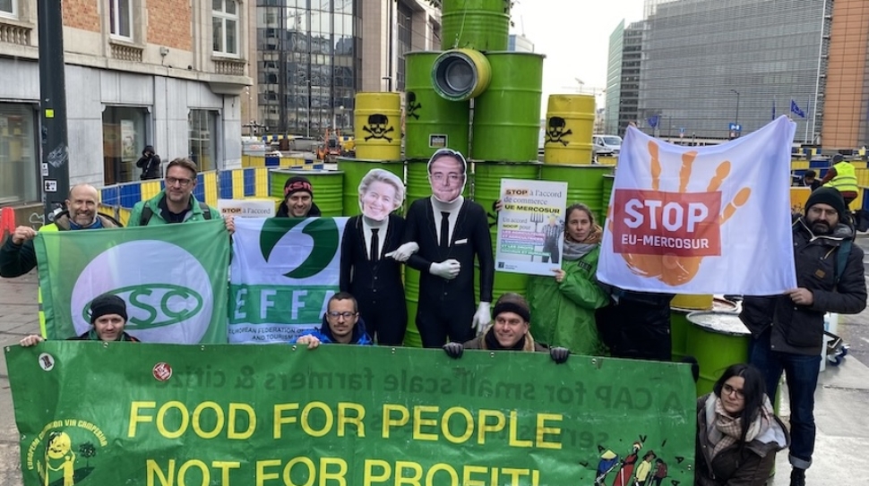 A groups of people holding protest banners standing in front of a stack of oil barrels
